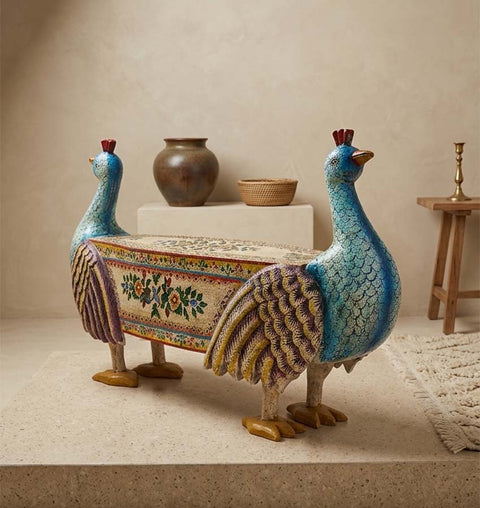 Hand-carved wooden accent bench shaped like two peacocks with intricate floral painting in blue, yellow, and beige.
Hand-painted decorative double peacock bench in a minimalist neutral room.
A rustic wooden indoor bench crafted in the shape of two facing-outward peacocks, detailed with hand-painted feather textures and traditional floral motifs.